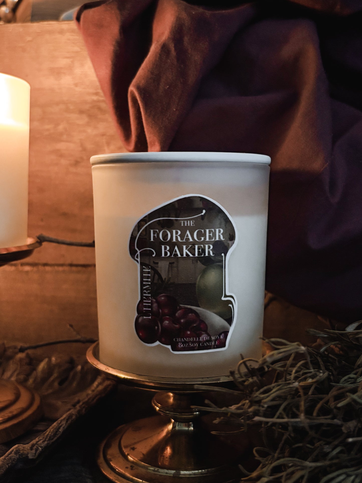 Candle with 'The Forager Baker' label on a decorative stand.
