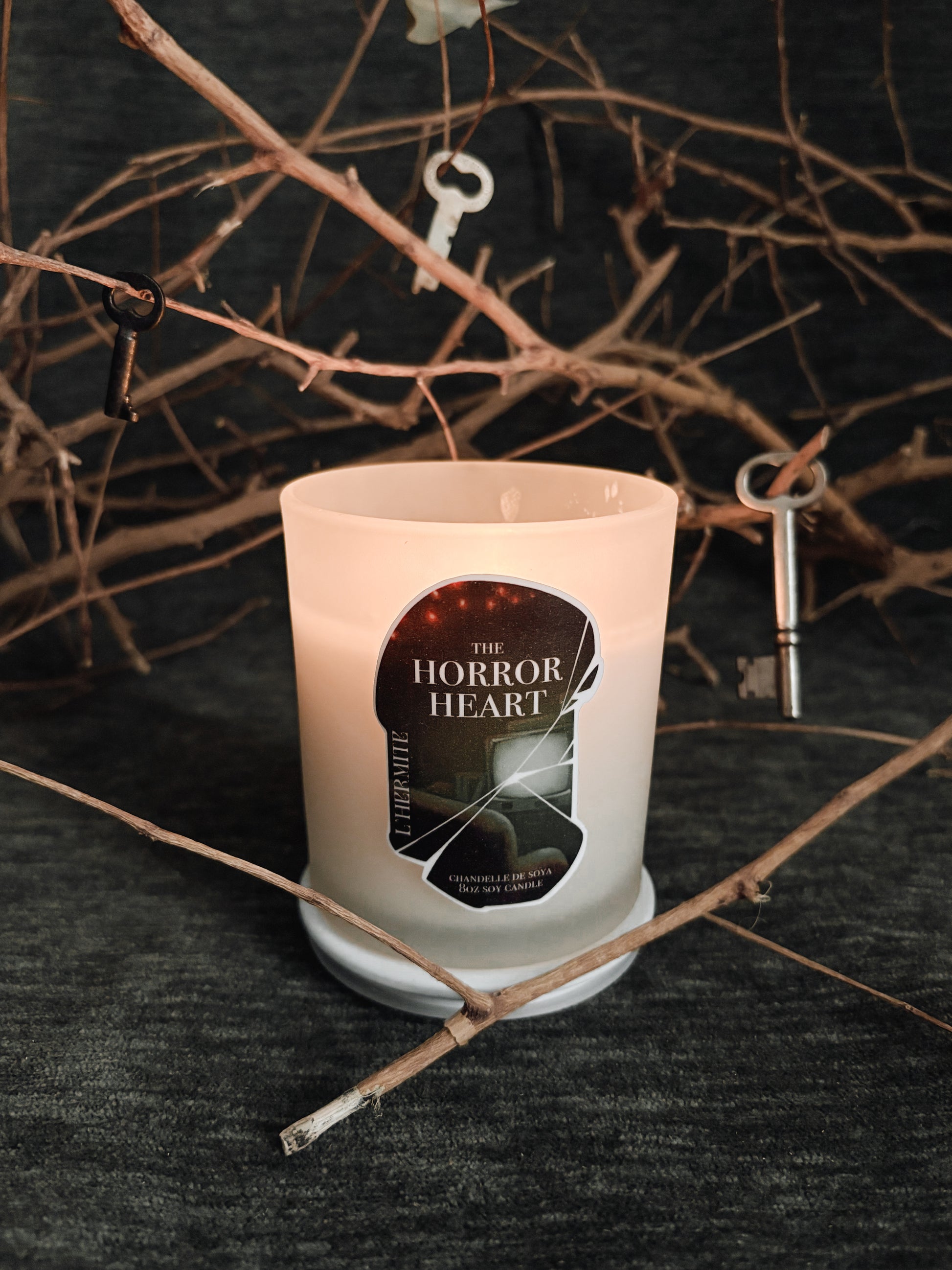 Candle with 'The Horror Heart' label on a dark background with branches and keys.