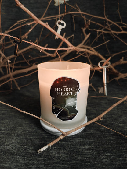 Candle with 'The Horror Heart' label on a dark background with branches and keys.