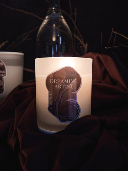 Candle with 'The Dreaming Artist' label on a dark fabric background