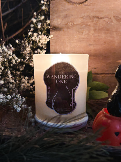 Candle labeled 'The Wandering One' with decorative elements on a wooden surface.