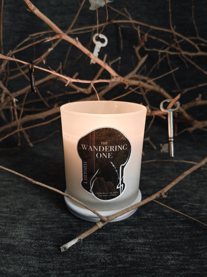 Candle with 'The Wandering One' label on a dark background with twigs and keys.