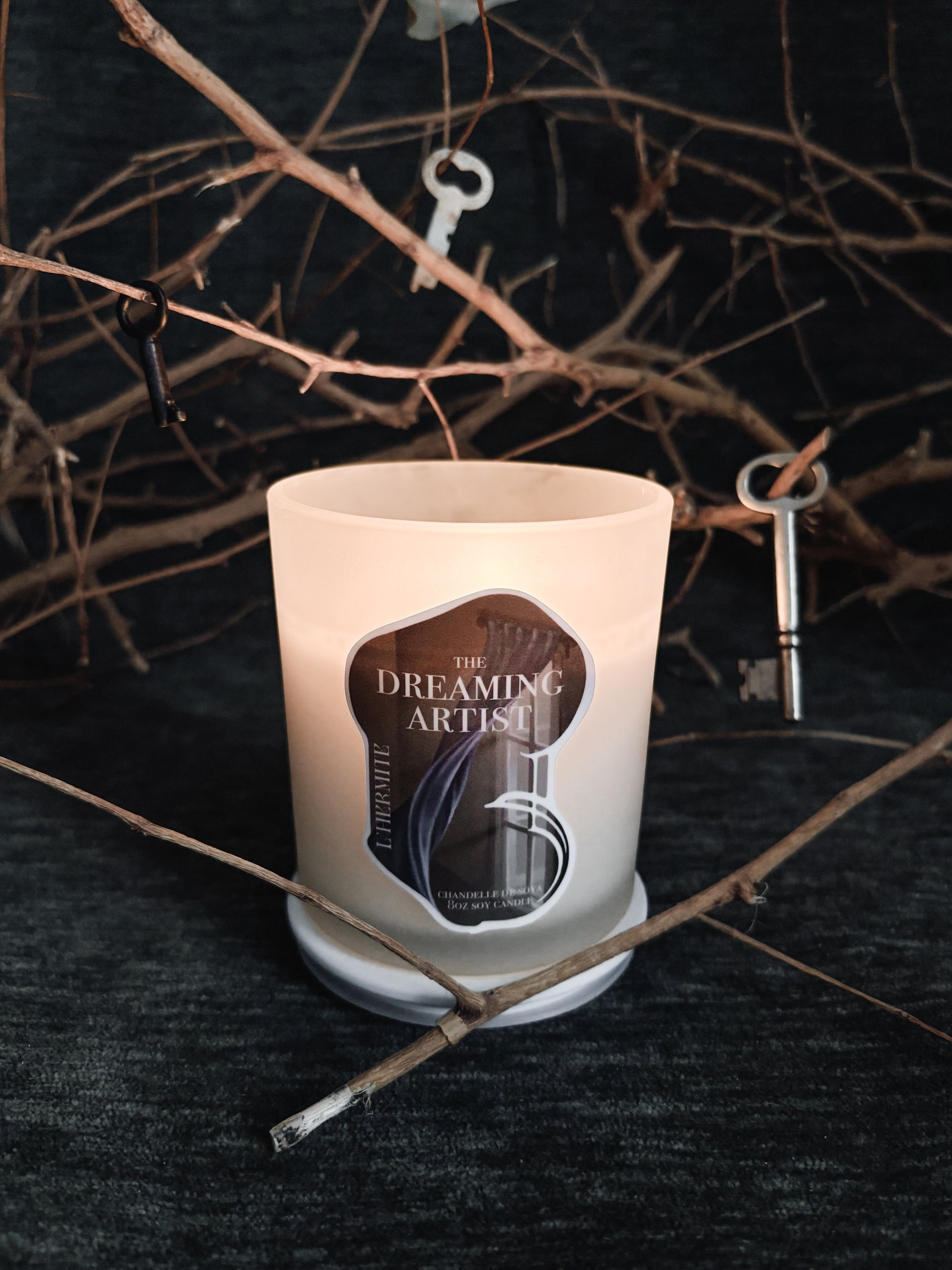 Candle with 'The Dreaming Artist' label on a dark background with branches.