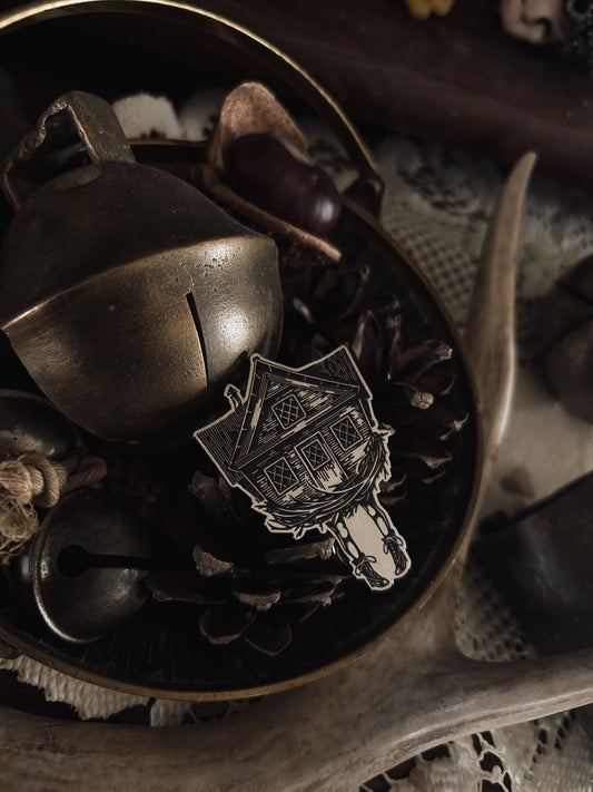 Glossy enamel pin shaped like a witchy wooden house on Victorian boots, referencing Baba Yaga and queer slang