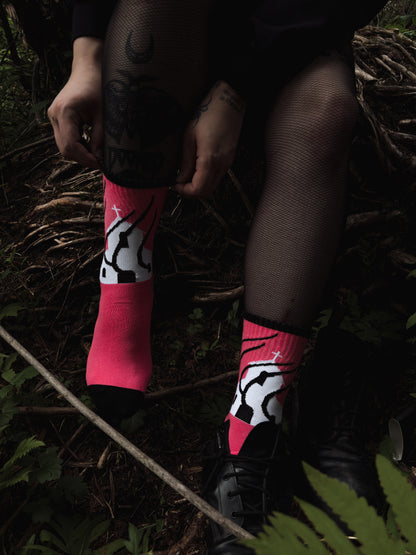 Hot pink socks featuring a flaming church design. Styled with fishnets and platform shoes, walking through mossy woods. A bold statement of queer defiance.