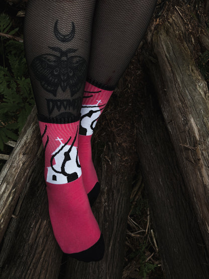 Hot pink socks featuring a flaming church design. Styled with fishnets and platform shoes, walking through mossy woods. A bold statement of queer defiance.